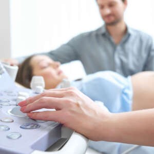 Selective focus on doctor hand operating ultrasound scanning machine pregnant couple on the background copyspace procedure treatment healthcare research medicine expecting childbirth parents.